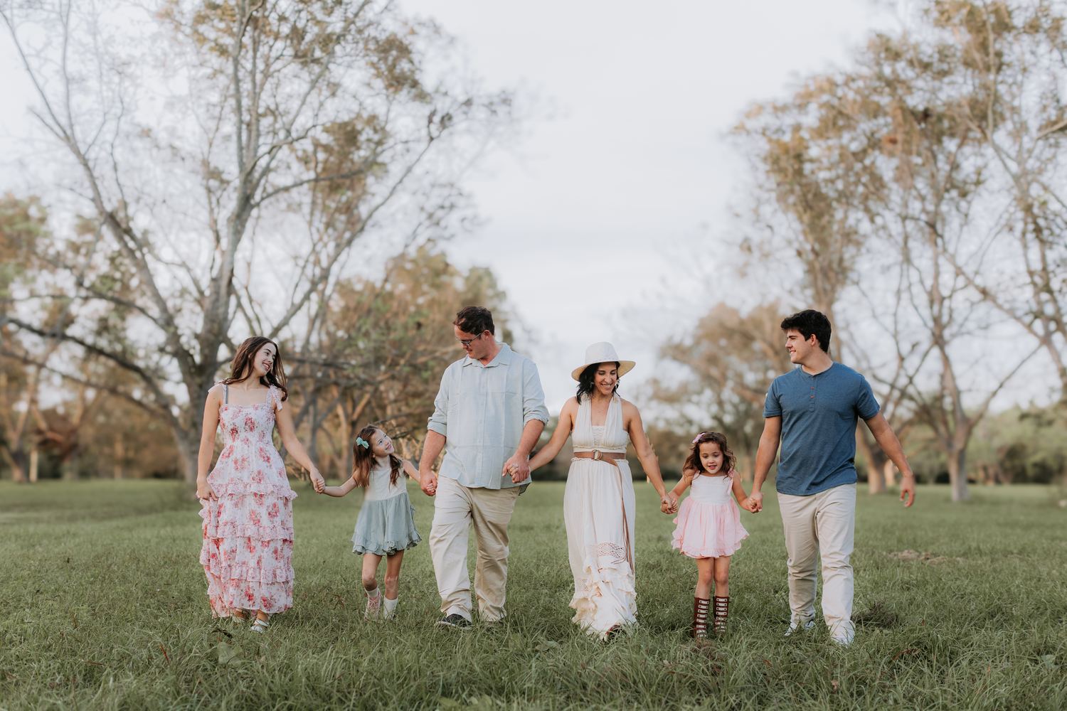 Monica Allen walking through a field at golden hour holding hands with her husband and their four children