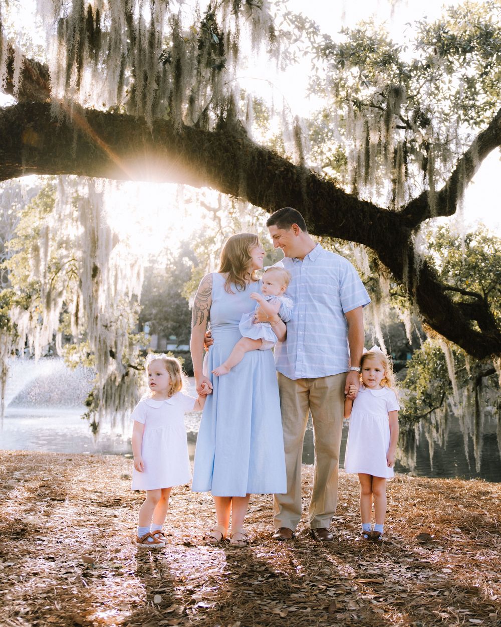 A family of five in soft blue beneath a moss-draped live oak beside the water at golden hour