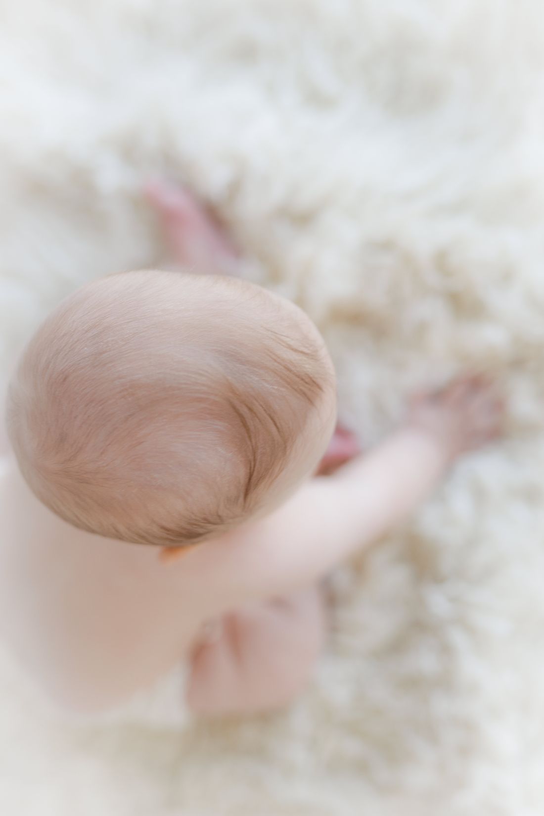 Overhead view of a baby's downy head as they sit on a cream sheepskin