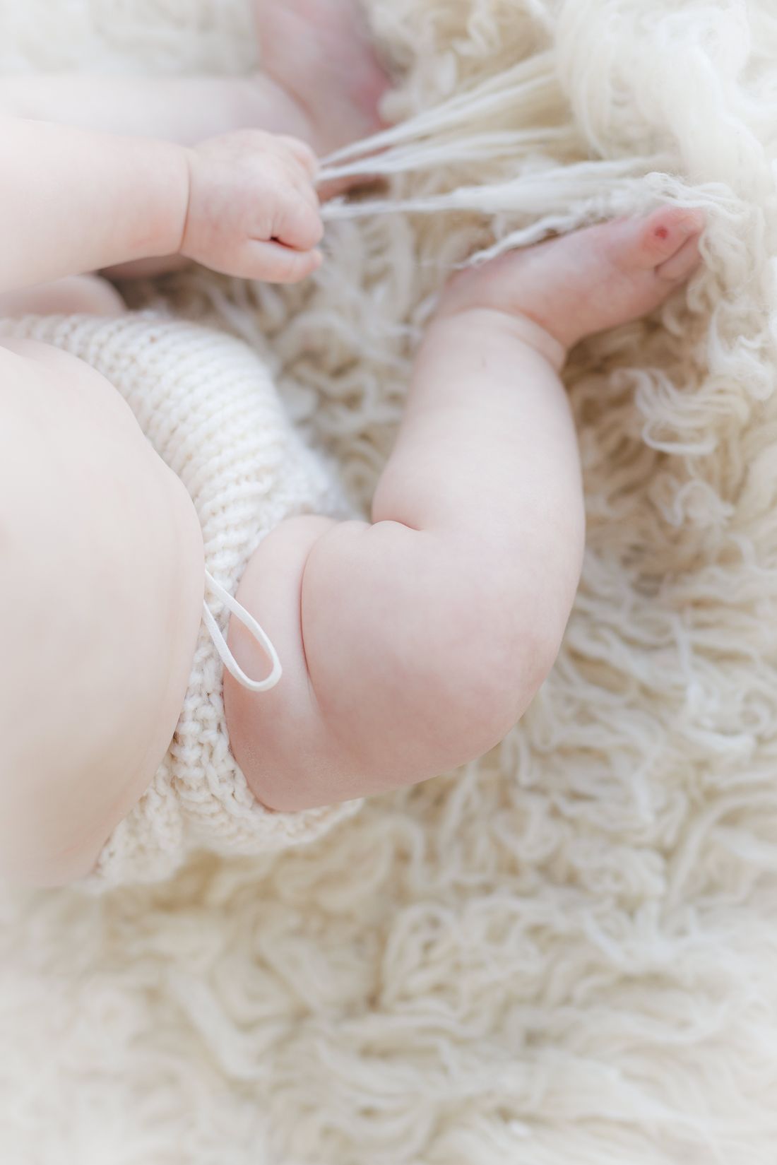 Close-up of a baby's rolls and bare feet in a knit romper on a soft rug