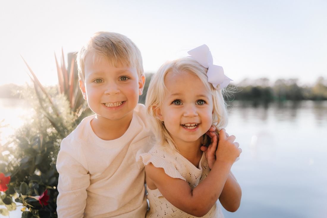 A brother and sister side by side in warm backlight at the water's edge