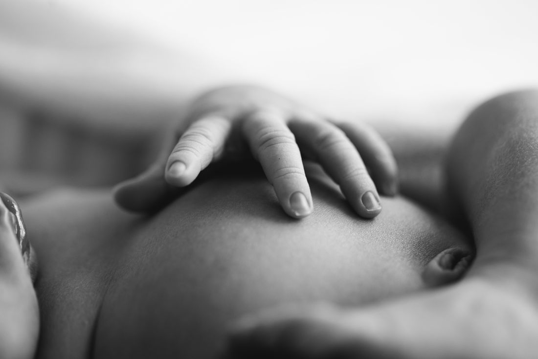 Black and white close-up of a newborn's hand resting open on his chest