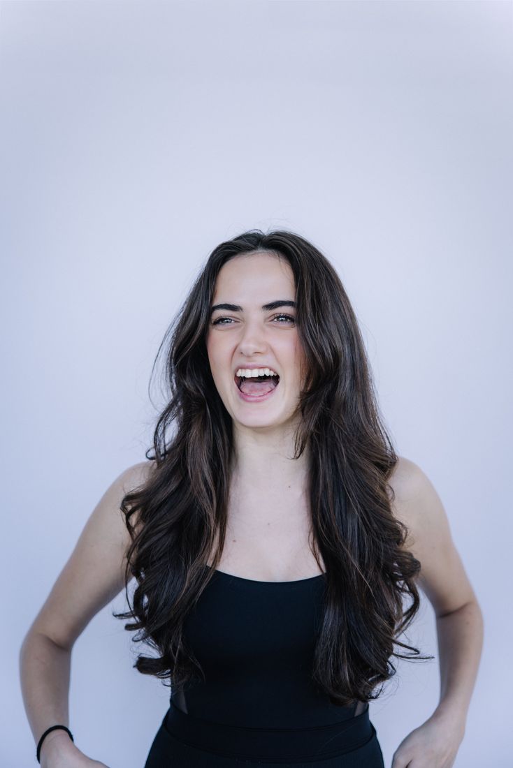 A young woman laughing at the camera against a plain studio backdrop