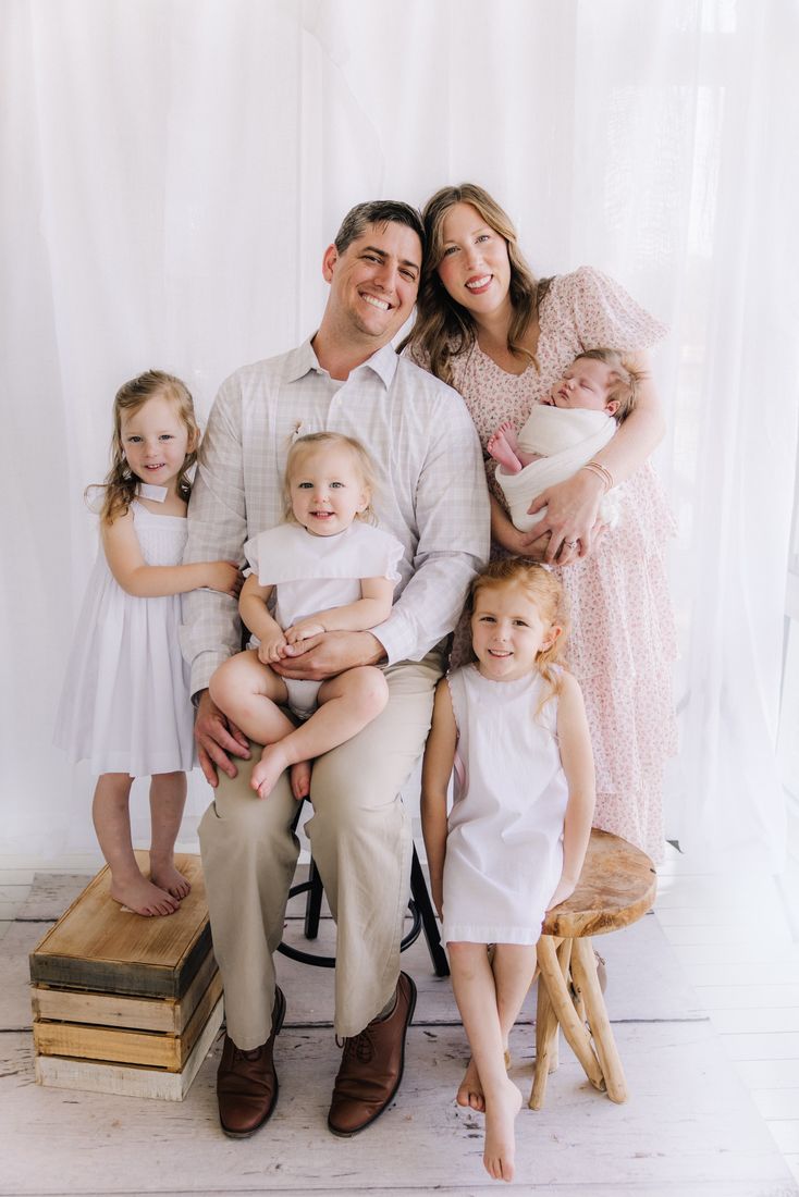 A family of six in soft neutrals in the studio, the mother holding her swaddled newborn