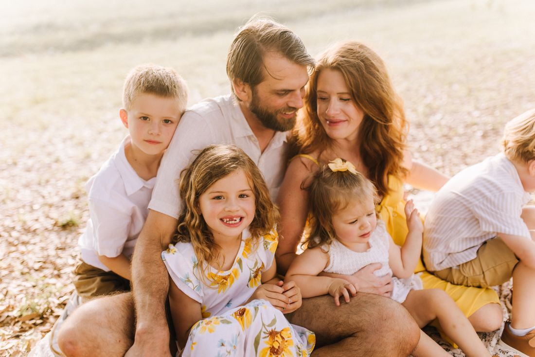 A family piled together in the grass, the parents looking down at the children in their laps