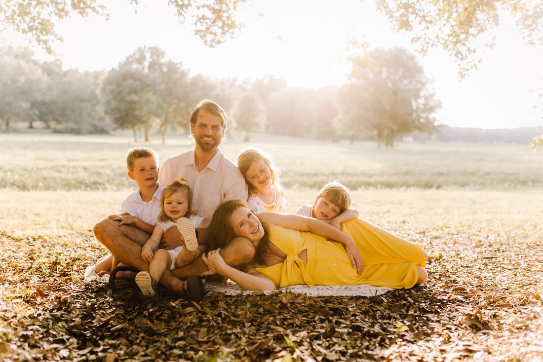 A family of six gathered on a blanket under the trees in the late afternoon sun