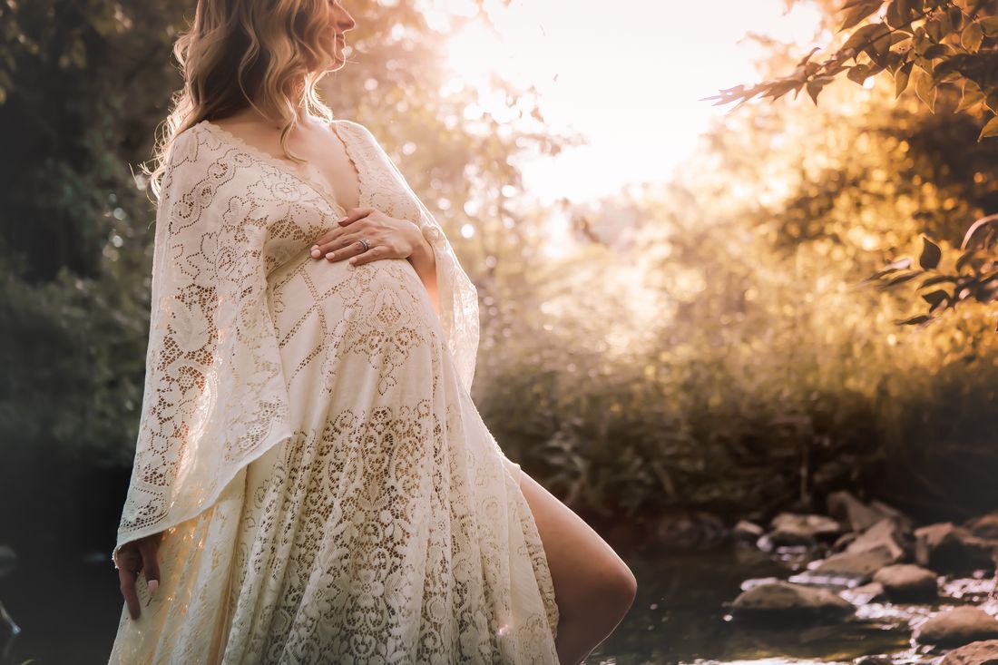 A close view of an expecting mother's hands on her belly, lace sleeves lit from behind by the low sun