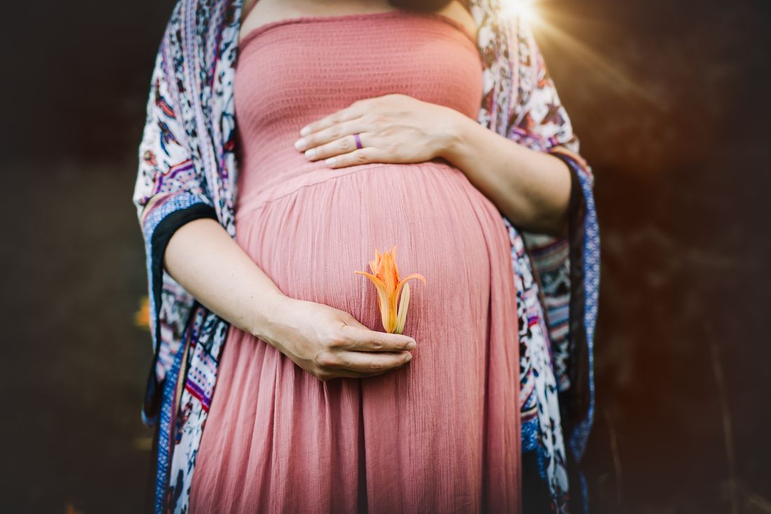 A close view of an expecting mother's hands cradling her belly, a single orange lily tucked between her fingers