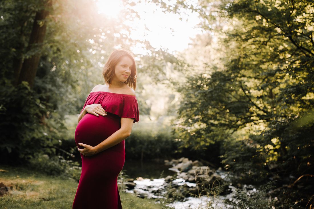 Two little sisters in flower crowns leaning against their expecting mother's belly, both smiling at the camera