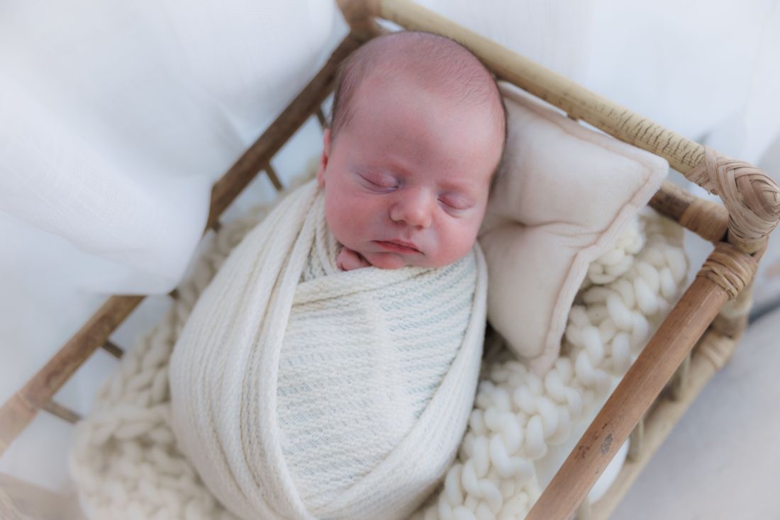Overhead view of a swaddled newborn asleep in a rattan bed with a small pillow