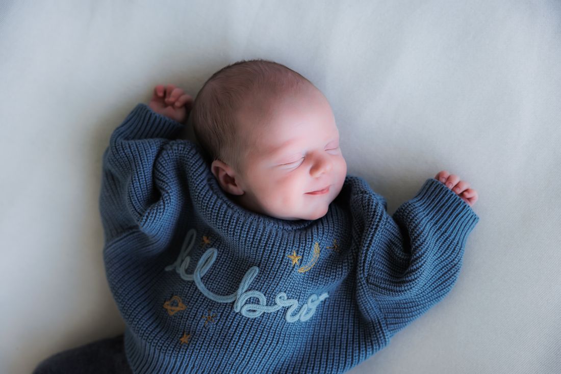 A newborn asleep in an oversized blue knit sweater embroidered with stars