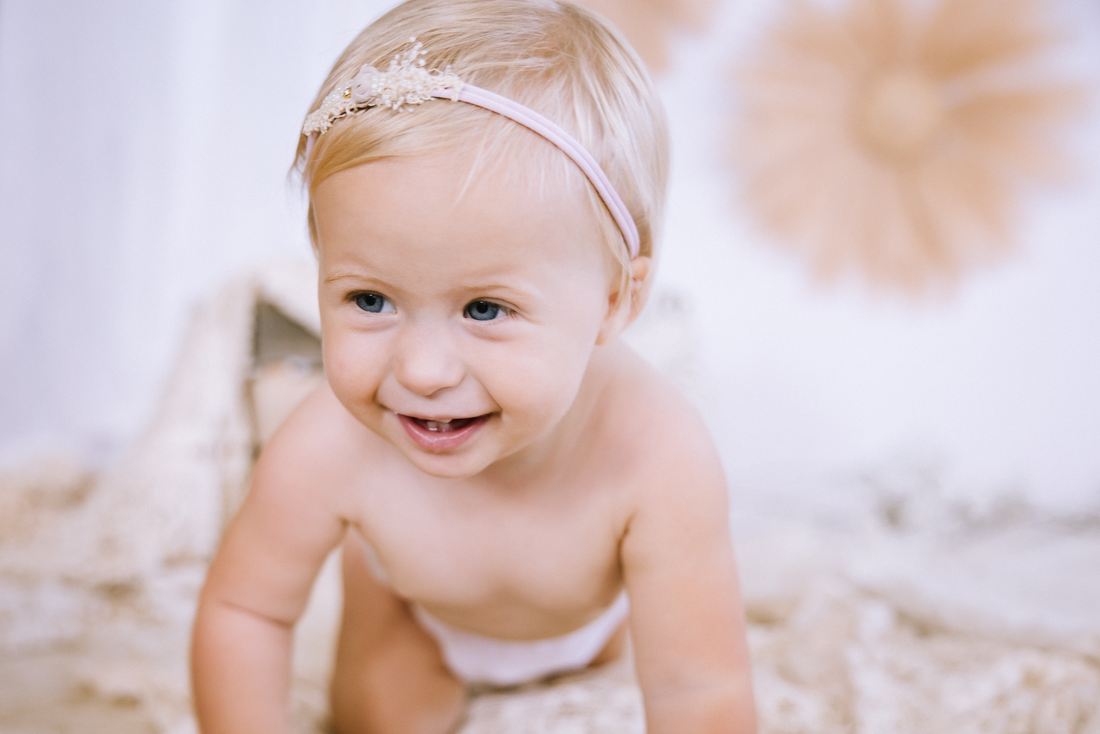 A crawling one-year-old in a flower headband smiling toward the camera