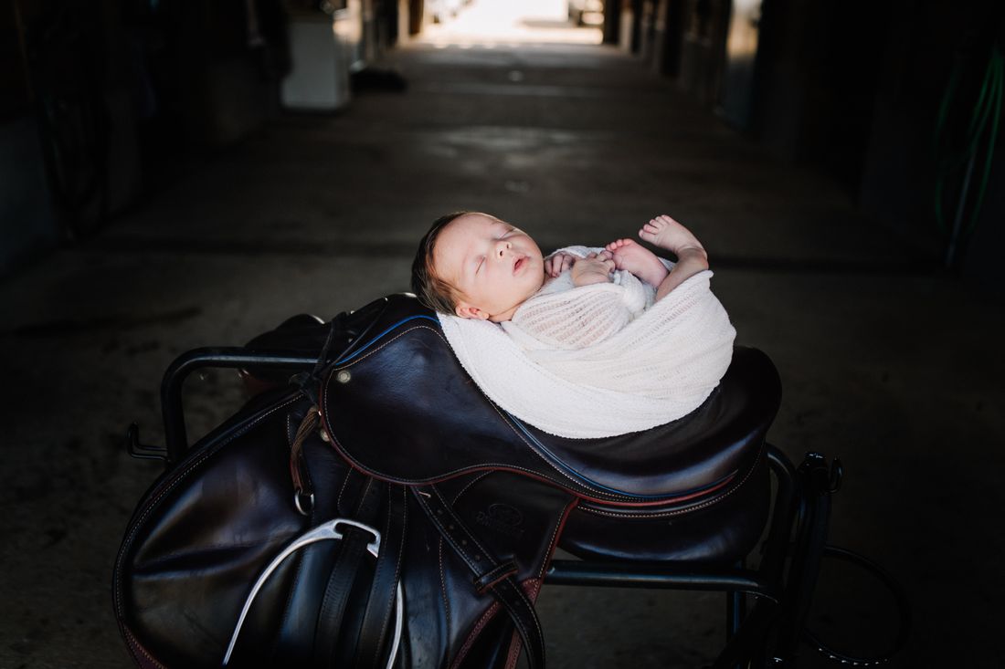 A closer view of a newborn asleep on a saddle, toes peeking out of the wrap