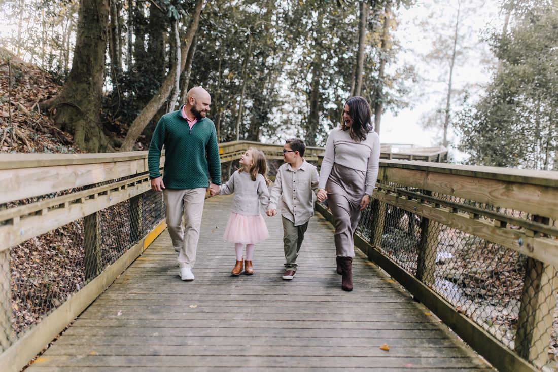 A family of four walking hand in hand along a wooden boardwalk through the trees