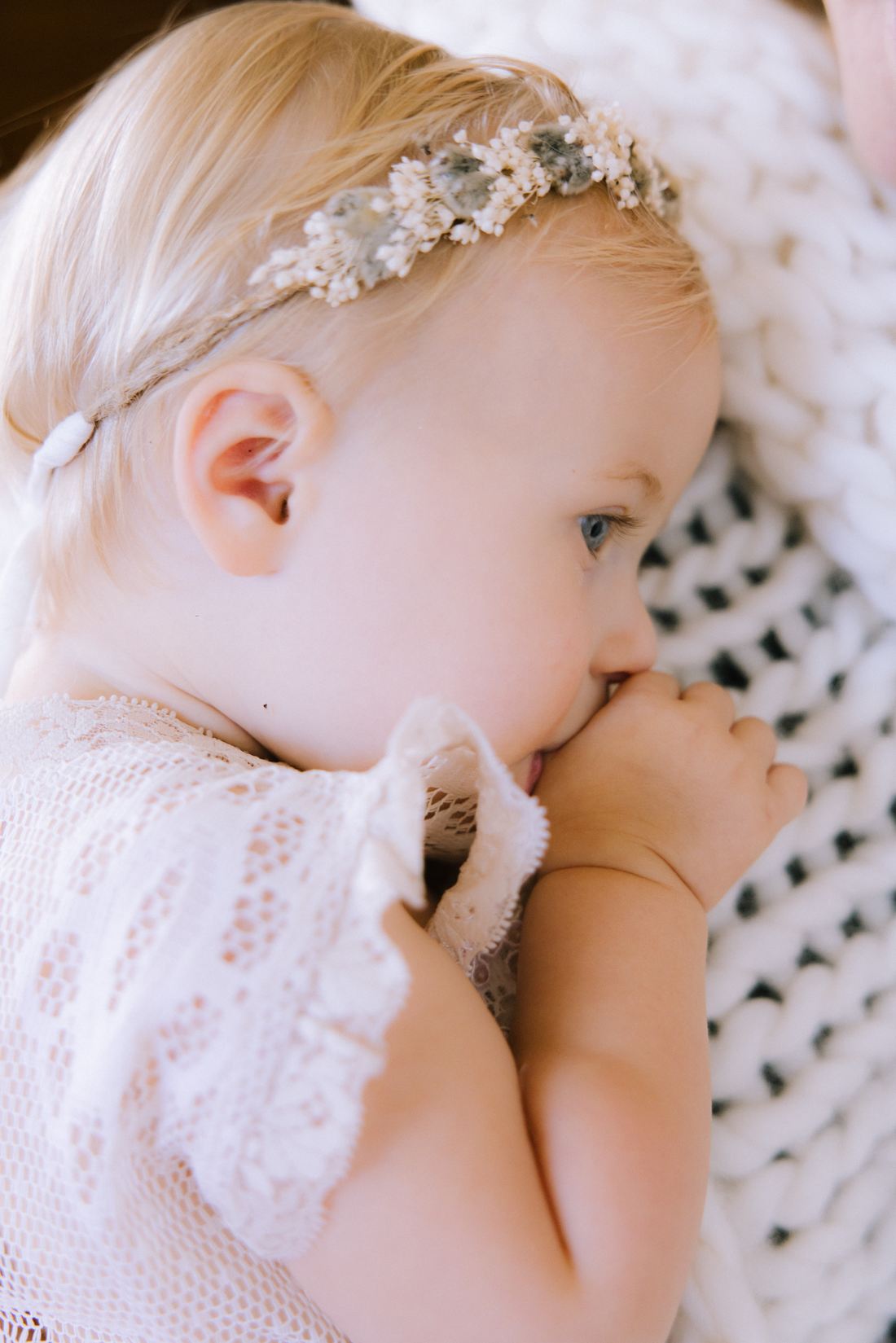 Profile of a baby in a dried-flower crown resting against a chunky knit throw