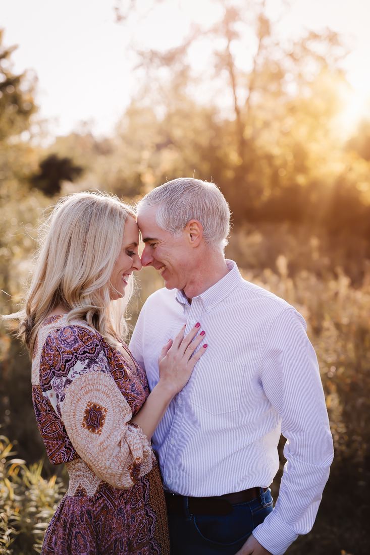 A husband and wife resting their foreheads together and laughing in a sunlit autumn field