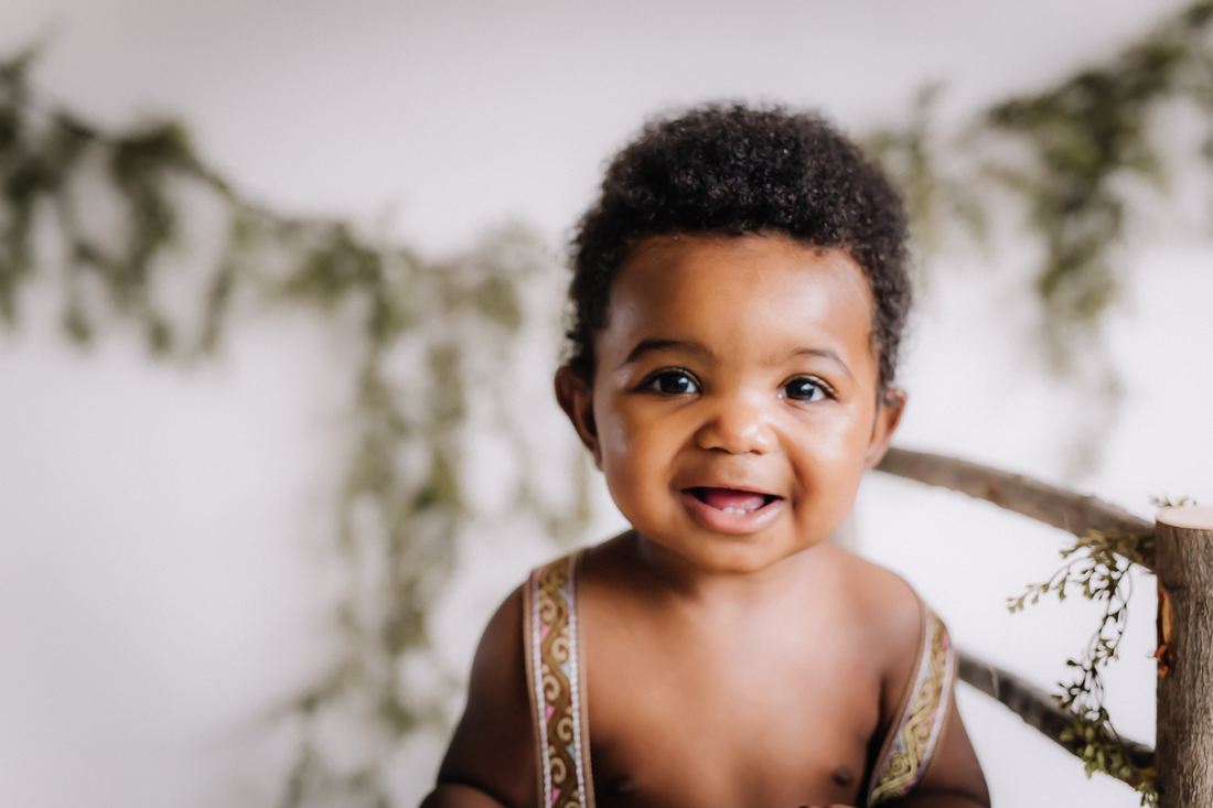 A baby boy grinning in front of a greenery garland in the studio