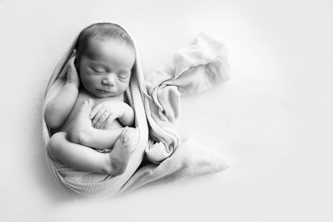 A newborn curled up asleep in a knit wrap