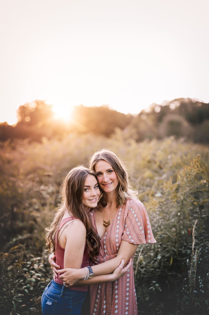 A mother and her teenage daughter holding each other cheek to cheek in a field of goldenrod at sunset