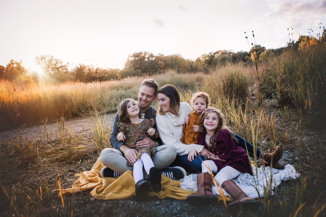 A family of six gathered on blankets in an autumn field, the parents in the middle with their four girls around them