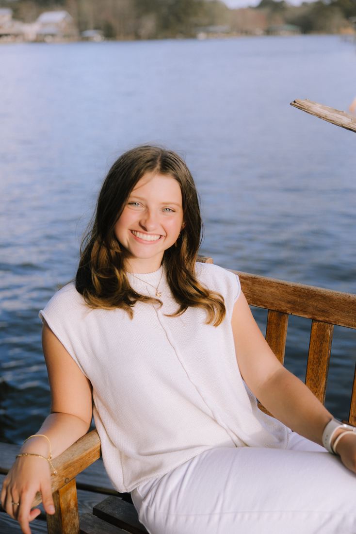 A senior seated on a wooden bench at the end of a pier, the bay and far shore stretching out behind her