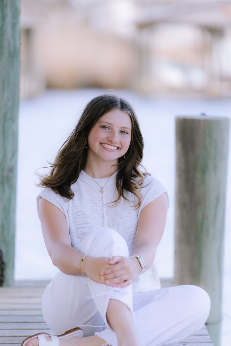 A senior sitting cross-legged on the dock between the pilings, arms around one knee
