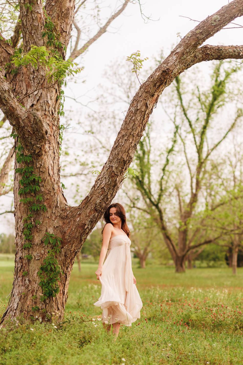 A senior standing beside a broad pecan trunk in a spring orchard