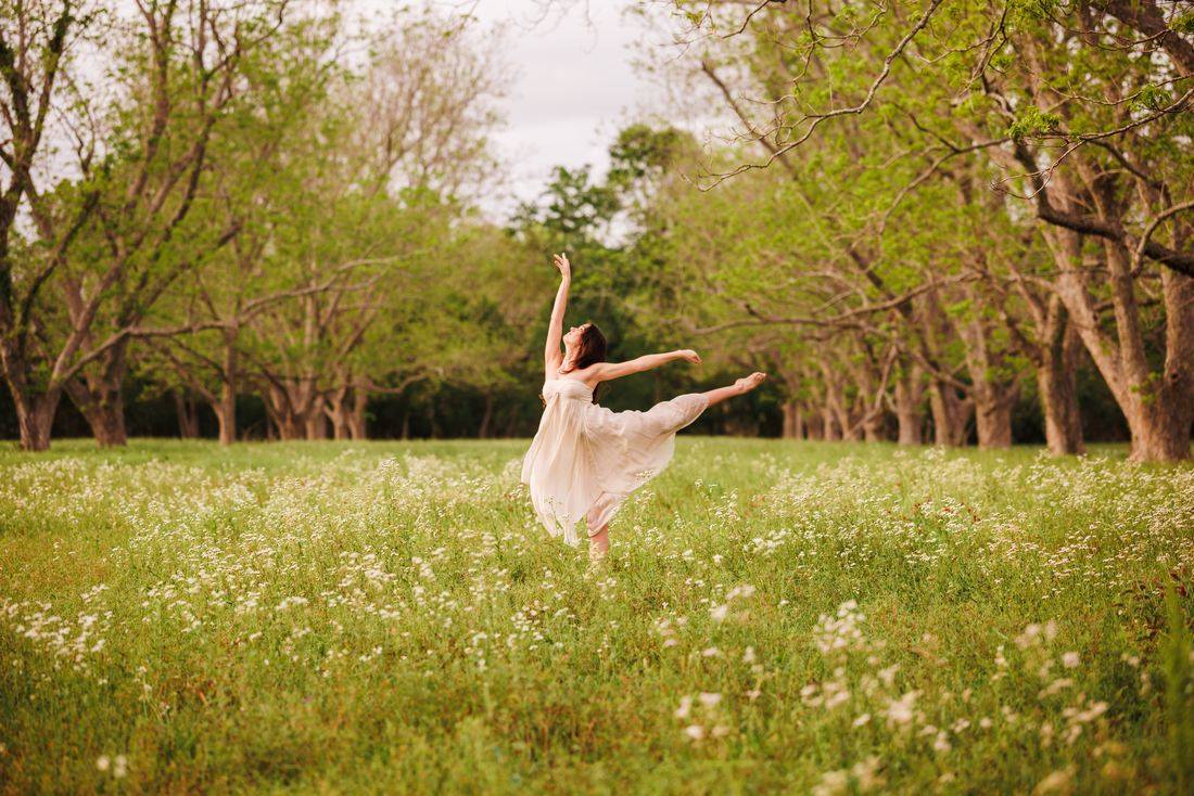 A senior in a flowing dress dancing barefoot through a field of wildflowers