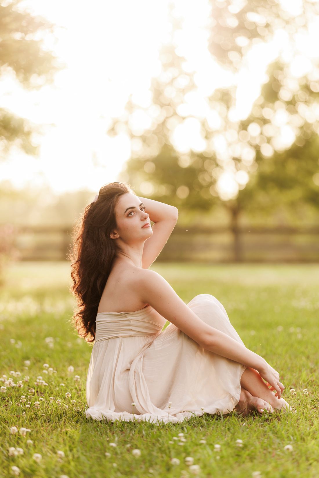A senior sitting in clover at golden hour with the light behind her