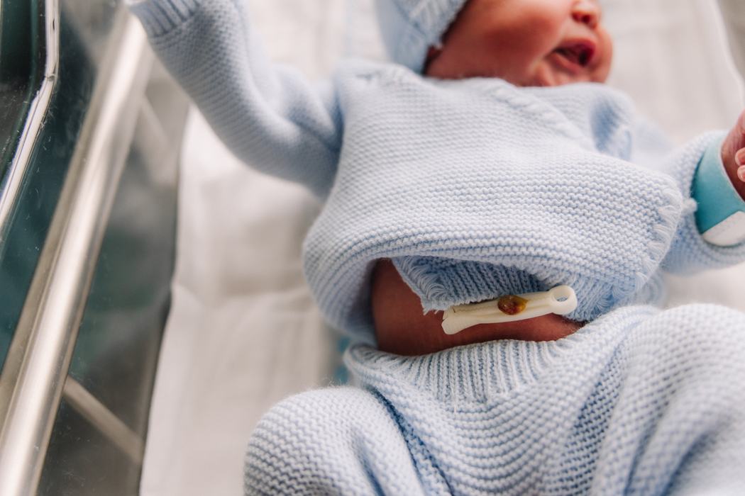 A newborn stretching in his hospital bassinet, cord clamp and knit blanket