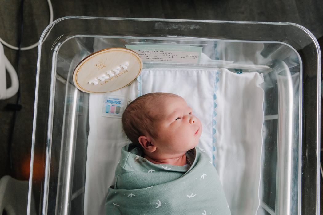A swaddled newborn lying in the hospital bassinet, seen from above