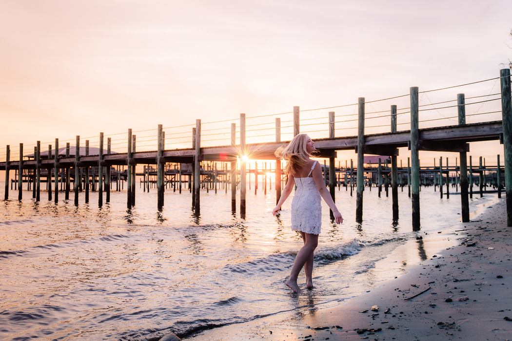 A senior walking barefoot through the shallows as the sun breaks under the pier