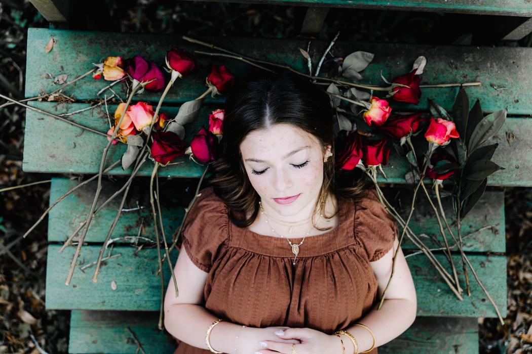 Overhead portrait of a senior lying on a green bench framed by scattered roses