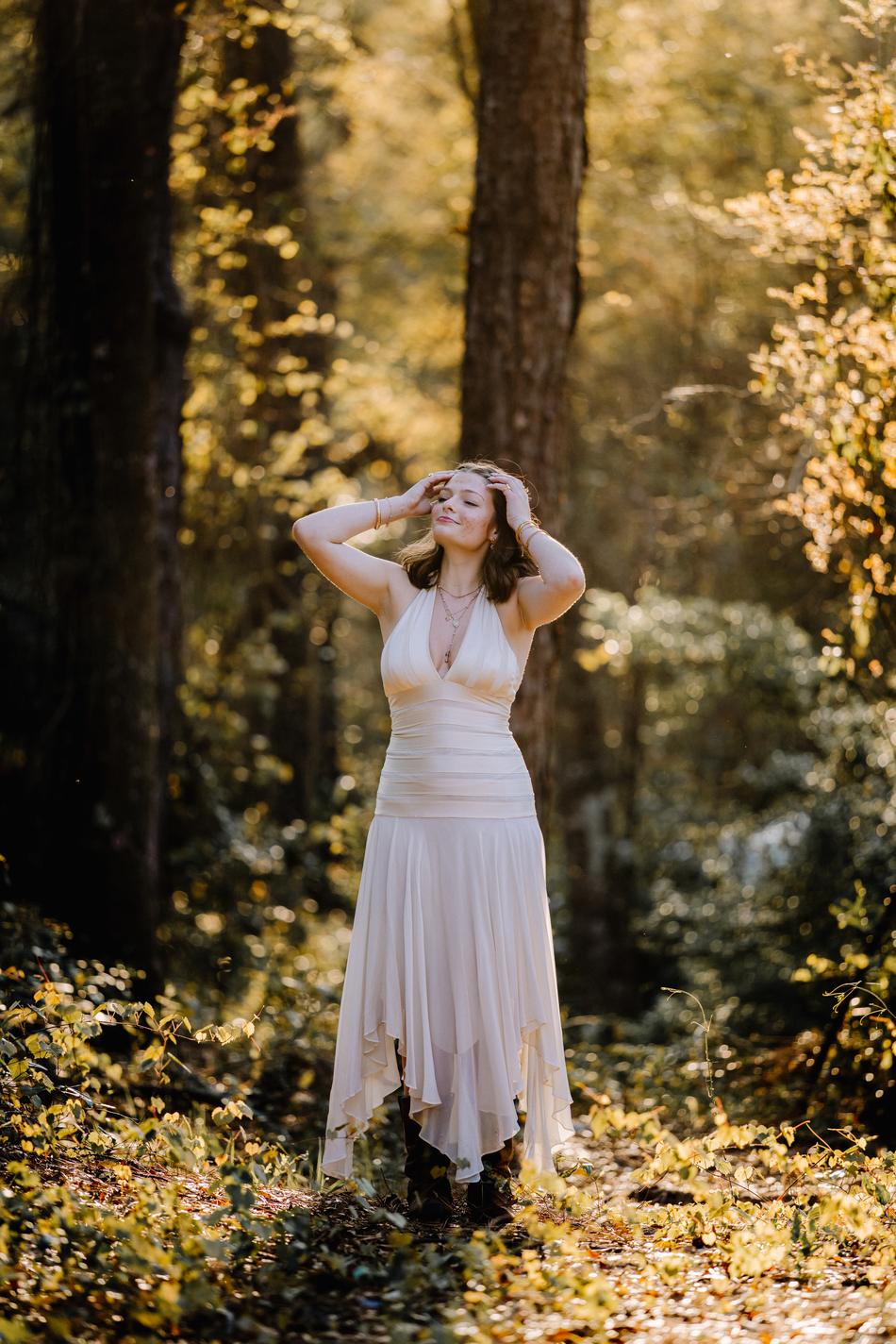 A senior in a long white dress among the trees