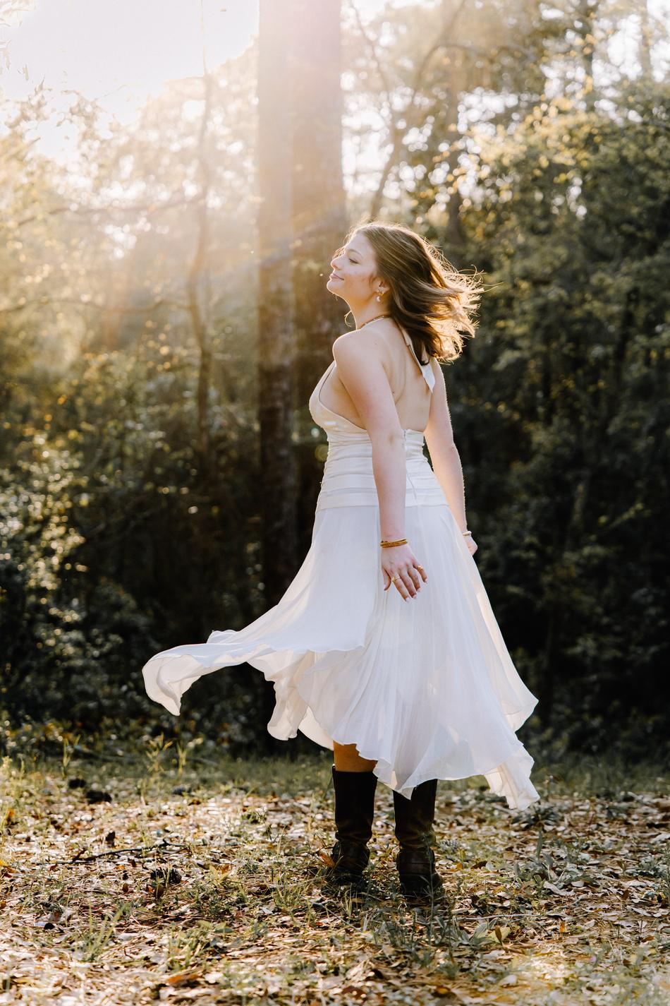 A senior in a white dress and boots turning so her skirt sweeps out behind her