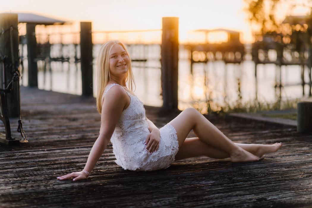 A senior sitting on the pier boards at sunset in a white lace dress