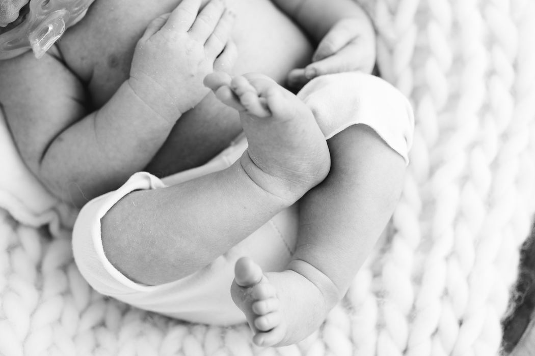 Black and white detail of a newborn's crossed legs and tiny hands
