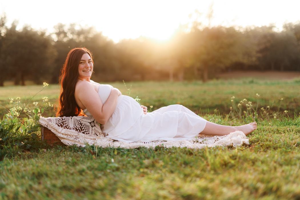 An expecting mother reclining on a lace blanket in a sunlit field