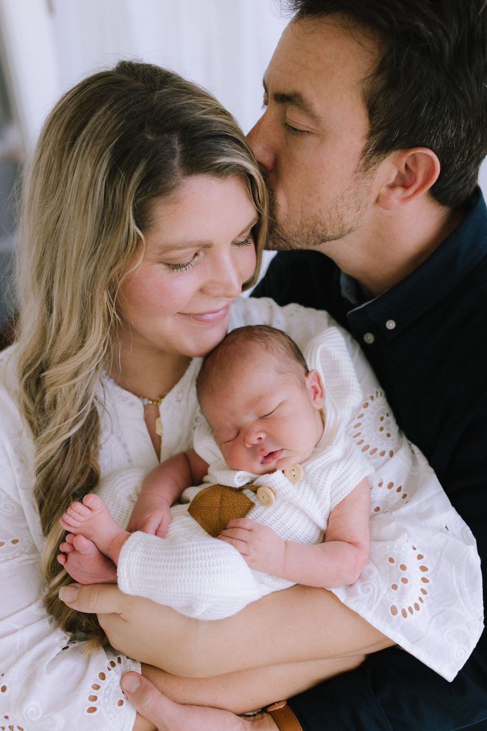 New parents holding their newborn together, the father kissing the mother's forehead