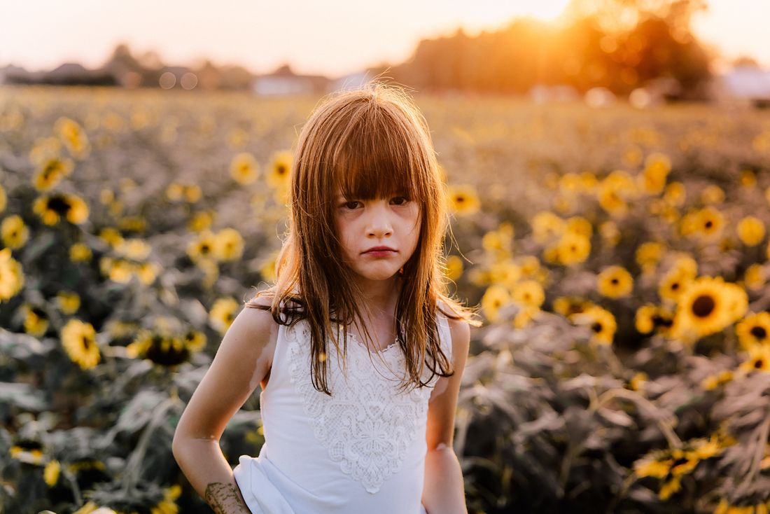 A girl in a white lace dress standing with her hands on her hips among the sunflowers