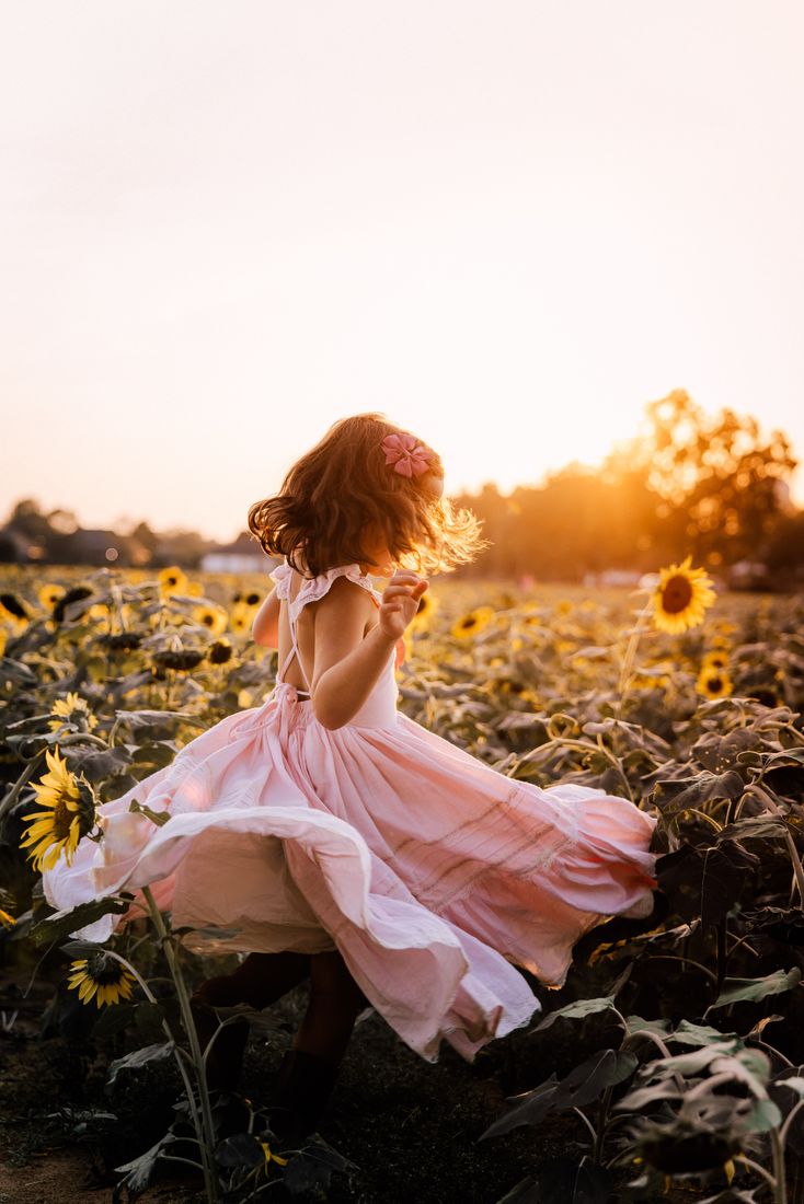 A girl in a pink dress spinning through the sunflowers, her skirt flaring out around her