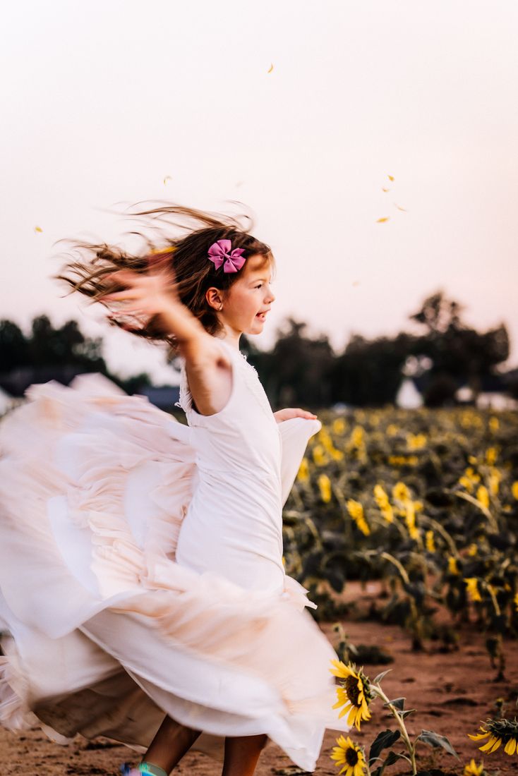 A girl running through the field in a cream dress, hair and skirt flying, petals in the air