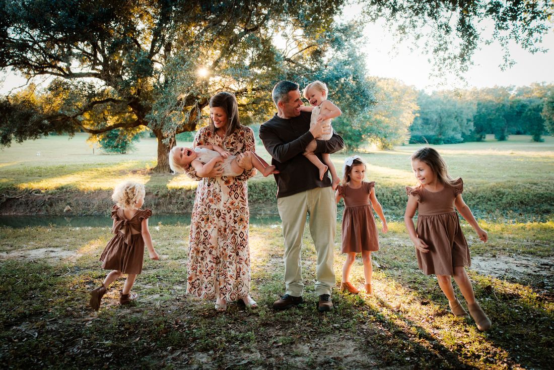 A family walking together beneath a spreading live oak, the children running ahead in the low sun