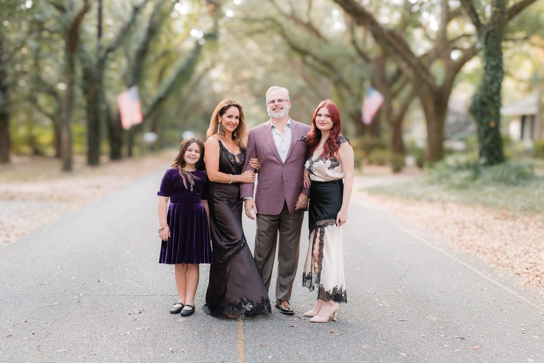 A family of four standing arm in arm in the middle of an oak-lined street