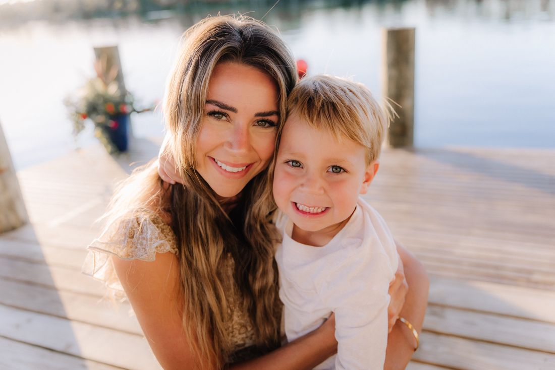 A mother and her young son cheek to cheek on a dock, both smiling at the camera