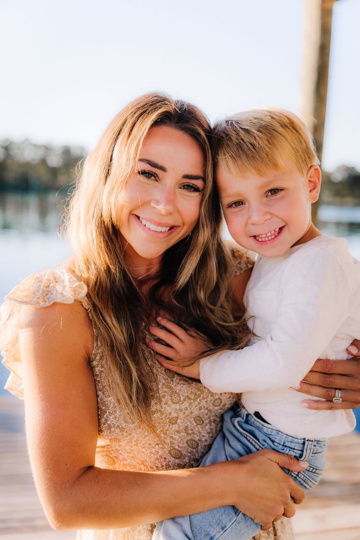 A mother holding her son on her hip at the end of a sunlit dock