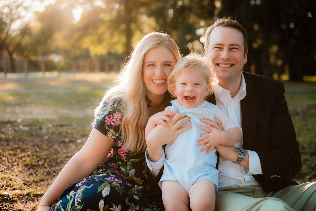 Parents sitting together in the grass with their laughing toddler between them