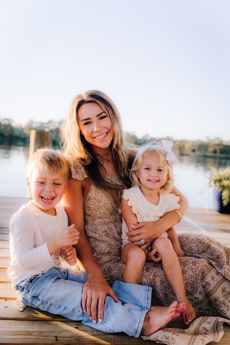 A mother sitting on a dock with her son and daughter tucked in on either side of her