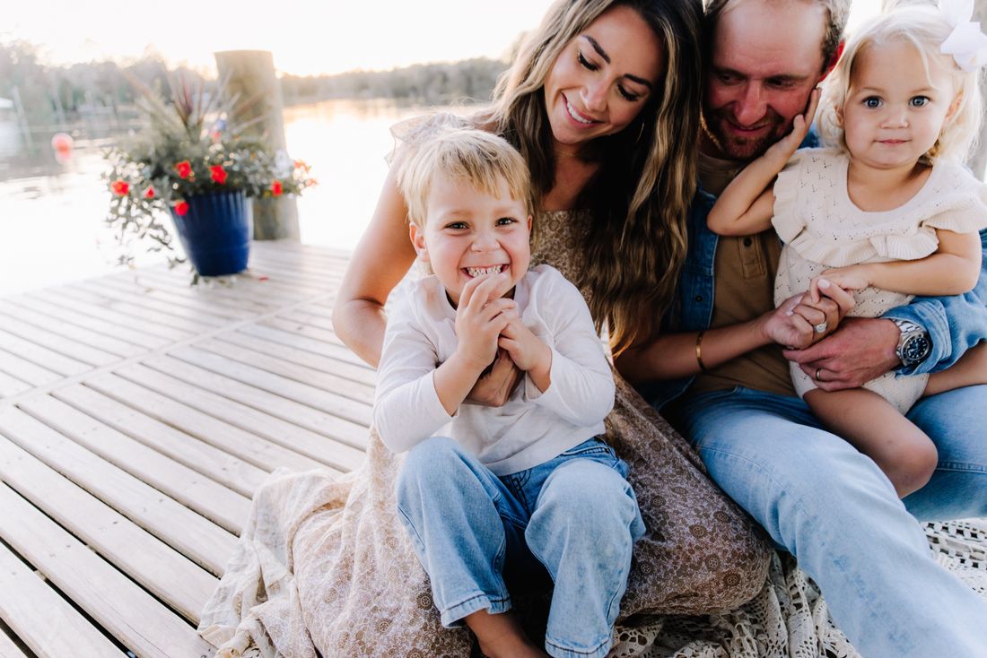 A family of four laughing together on the dock, the little boy grinning at the camera
