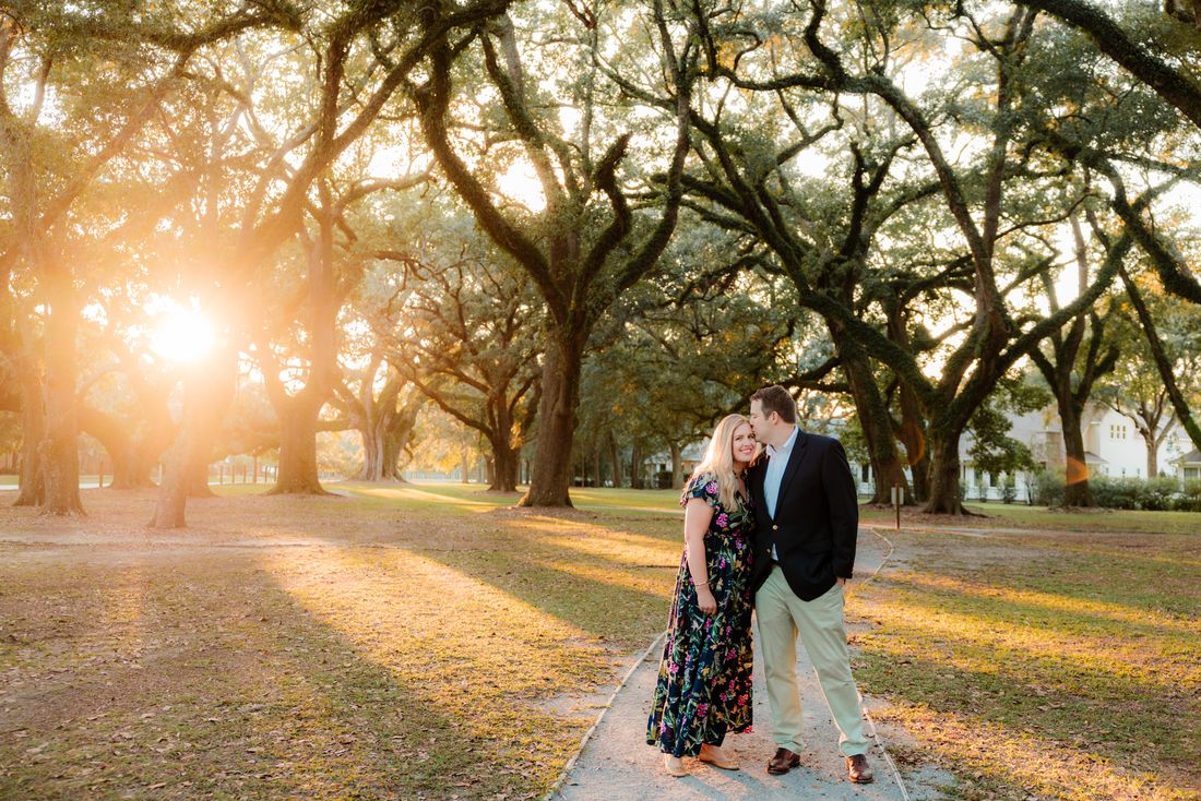 A couple embracing beneath an avenue of live oaks as the sun drops behind them